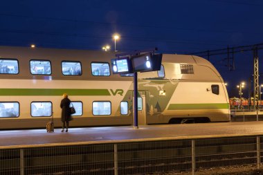 Kouvola, Finlandiya - 8 Kasım 2018: Uzun pozlama fotoğraf. Geceleri tren istasyonu üzerinde. Bulanık kadın platformu üzerinde kalan seyahat çantası.