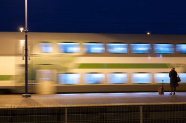 Kouvola, Finlandiya - 8 Kasım 2018: Uzun pozlama fotoğraf. Hareket istasyonunda gece tren. Bulanık kadın platformu üzerinde kalan seyahat çantası