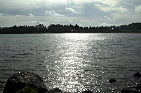 Темное Сверкающее Озеро Камнями Берегу Находится Голубым Небом Облаками Освещенными — стоковое фото
