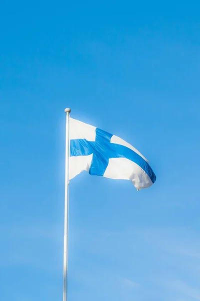 Nationale vlag van Finland op pole-position op wind op blauwe hemelachtergrond. — Stockfoto