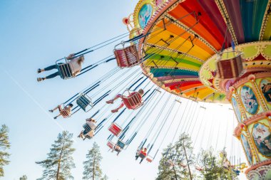 Kouvola, Finland - 18 May 2019: Ride Swing Carousel in motion in amusement park Tykkimaki and aircraft trail in sky. clipart