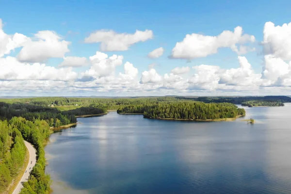 Widok z lotu ptaka na jezioro z wyspą, drogą i lasem w letni słoneczny dzień w Finlandii. Fotografia dronów — Zdjęcie stockowe
