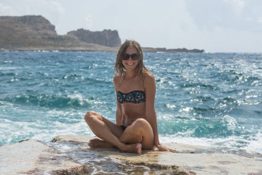 Portre. Büyük bir kayanın üzerinde oturan genç kadın ve mesafe içine deniz görünüyor. Seçici yumuşak odak. Mutlu yaz günlerinde. Balos lagün. Elafonisi Beach - Girit, Yunanistan görüntü