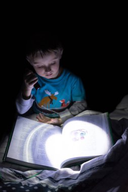 Evde el feneri ile gece bir kitap okuma eğlenceli beyaz çocuk. Çocuk okuma masal, karanlık fotoğraf.