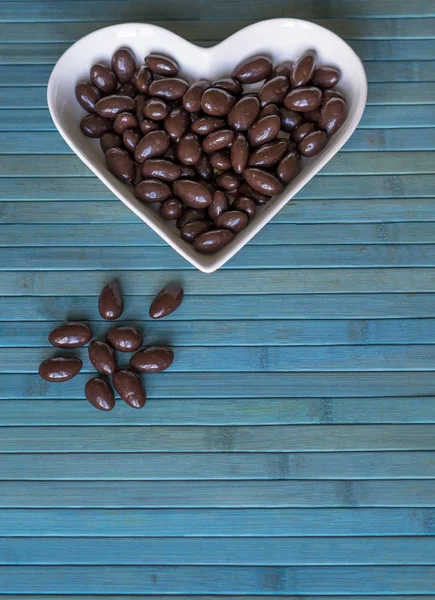 Орехи расположены в форме сердца на заднем плане. Изображение еды закрывает конфеты, шоколадное молоко, экстра темные миндальные орехи. Текстура любви — стоковое фото