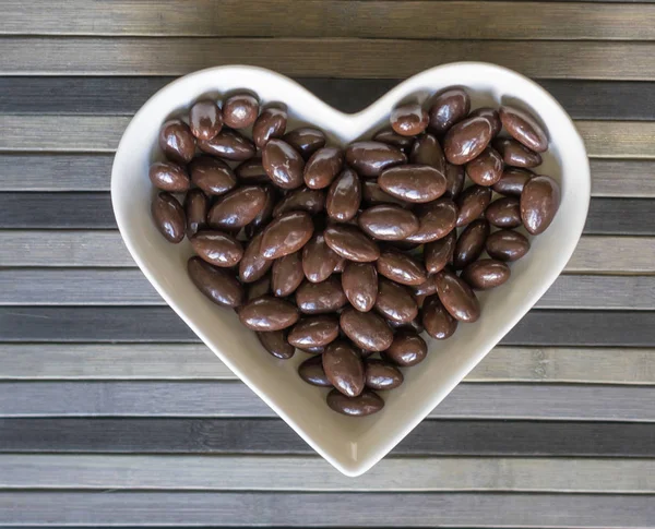 Орехи расположены в форме сердца на заднем плане. Изображение еды закрывает конфеты, шоколадное молоко, экстра темные миндальные орехи. Текстура любви — стоковое фото