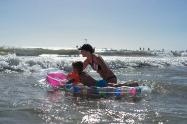 Mutlu bir aile yaşam tarzı. Gülümseyen genç anne ve oğlu atlama ve dalgalar kırma eğlenceli ile sıçrayan.