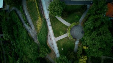 Polonya 'nın Plock kentindeki bir parkın tepeden aşağı insansız hava aracı görüntüsü. Ağaçlar, yürüyüş yolları ve insanlarla çevrili dairesel bir çatısı var. Güneşli bir bahar gününde çekilen görüntüler yeşilliği ve kentsel manzara tasarımını yemyeşil gösteriyor..