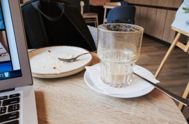 Laptop bir tabak yemek ve bir bardak sütle bir masanın üzerinde. Tabakta bir çatal ve masada bir kaşık var.