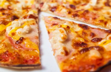 Jambon ve peynirli bir dilim pizza. Dilim ikiye bölünmüş. Pizza beyaz tabakta.