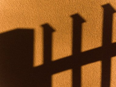 Duvarda bir çitin gölgesi var. Gölge dört direkli bir çitin gölgesi.