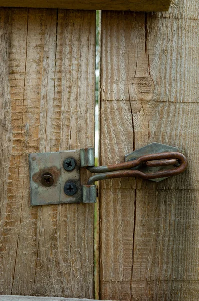 Paslı kapı mandalı ahşap bir çite bağlı. Kapı mandalı eski ve paslı, ahşap yıpranmış ve yıpranmış. Kapı açık ve mandal da güvenli değil. Sahne biraz uğursuzdur.