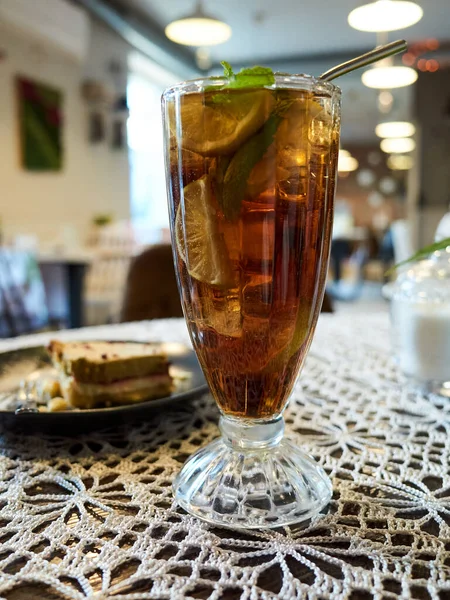 Bir bardak kireç dilimli çay masanın üzerinde duruyor. Masa dantel altlık ve bir tabak yemekle kaplı.