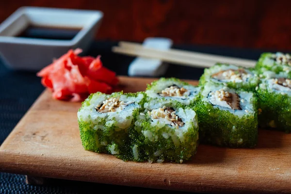 Yeşil yosun ambalajı ve kırmızı garnitürlü bir tabak suşi. Suşi ahşap bir masada oturuyor.