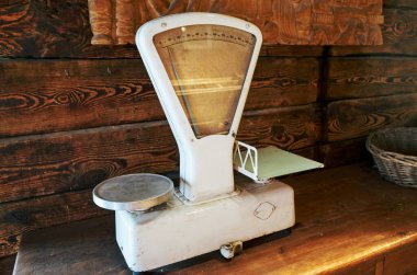 Eski bir tartı ahşap bir masada oturur. Terazi beyaz ve siyah tabanlı. Pul eski ve eski bir görünümü var.