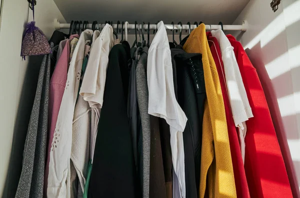 Dolapta kırmızı bir kazak ve beyaz bir gömlek var. Giysiler askıda asılı duruyor ve askıda da bir lavanta kesesi var. Sahne dağınık ve dağınık.