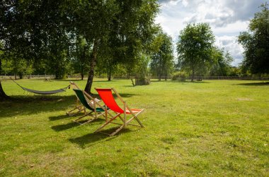 Çimenli bir tarlada iki katlanabilir sandalye oturuyor. Biri kırmızı ve diğeri yeşil.