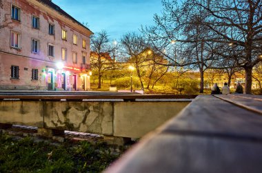 Bench kırmızı çatılı bir binanın önünde. Yedek kulübesi boş. Gökyüzü karanlık ve sokak ışıkları açık. Varşova 'daki eski kasaba. Varşova 13.04.2025 Polonya