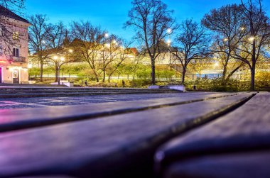 Park yeri ve arka planda ağaçlar. Yedek kulübesi boş. Gökyüzü karanlık ve ışıklar açık. Varşova 'daki eski kasaba. Varşova 13.04.2025 Polonya