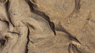 Kumsal kum dokusu. Geniş, dalgalı, kısa yatay çizgiler, dalgalanmalar ve rüzgarın oluşturduğu desenlerle dokulu bir kum yüzeyinin yakın çekimi. Renkler ışıktan koyu kahverengiye değişir.
