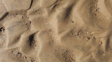 Kumsal kum dokusu. Geniş, dalgalı, kısa yatay çizgiler, dalgalanmalar ve rüzgarın oluşturduğu desenlerle dokulu bir kum yüzeyinin yakın çekimi. Renkler ışıktan koyu kahverengiye değişir.