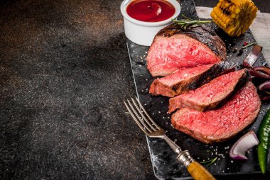 Taze ızgara sığır eti, ev yapımı barbekü et orta pişmiş, baharatlar, koyu arka plan, kopya alanı ile siyah taş kesme tahtası üzerinde