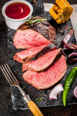 Taze ızgara sığır eti, ev yapımı barbekü et orta pişmiş, baharatlar, koyu arka plan, kopya alanı ile siyah taş kesme tahtası üzerinde