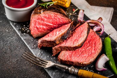 Taze ızgara sığır eti, ev yapımı barbekü et orta pişmiş, baharatlar, koyu arka plan, kopya alanı ile siyah taş kesme tahtası üzerinde