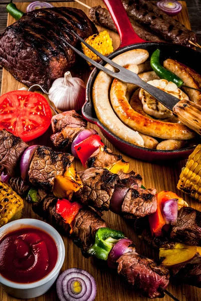 Assortment various barbecue food grill meat, bbq party fest - shish kebab, sausages, grilled meat fillet, fresh vegetables, sauces, spices, on old wooden rustic table, above copy space