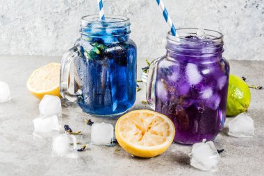 Sağlıklı yaz soğuk içecek, buzlu organik ve menekşe mavi kelebek bezelye çiçeği çayı limes ve limon, gri beton arka plan kopya alanı üstten görünüm