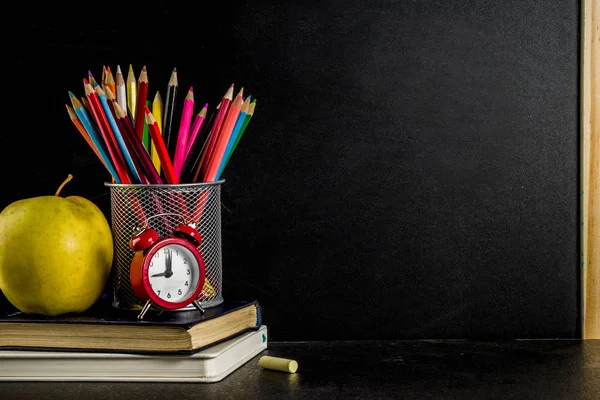 Kitaplar, çalar saat, renkli kalemler, kara tahta arka plan ile okul kavramı geri