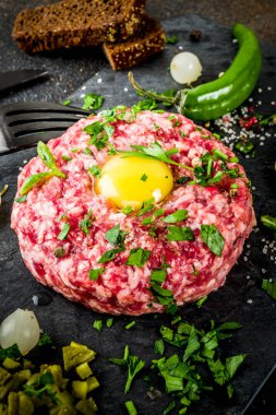 Fransız mutfağı, sığır eti biftek tartare çiğ Bıldırcın yumurta sarısı, salatalık turşusu ve soğan, taze otlar, ekmek, karanlık paslı arka plan kopya alanı ile