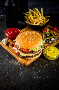 Çeşitli parti gıda, hamburger, patates kızartması, patates cipsi, salatalık turşusu, soğan, domates ve soğuk bira şişeleri, paslı siyah beton arka plan kopya alanı