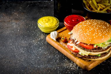 Çeşitli parti gıda, hamburger, patates kızartması, patates cipsi, salatalık turşusu, soğan, domates ve soğuk bira şişeleri, paslı siyah beton arka plan kopya alanı