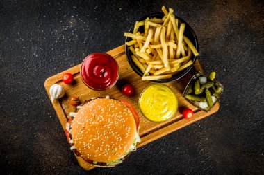 Çeşitli parti gıda, hamburger, patates kızartması, patates cipsi, salatalık turşusu, soğan, domates ve soğuk bira şişeleri, paslı siyah beton arka plan kopya alanı