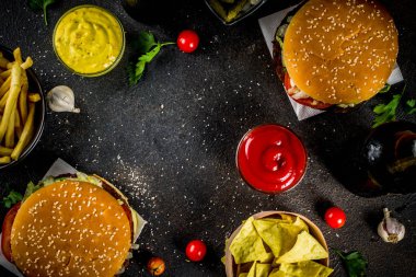 Çeşitli parti gıda, hamburger, patates kızartması, patates cipsi, salatalık turşusu, soğan, domates ve soğuk bira şişeleri, paslı siyah beton arka plan kopya alanı