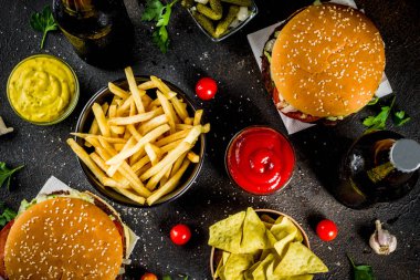 Çeşitli parti gıda, hamburger, patates kızartması, patates cipsi, salatalık turşusu, soğan, domates ve soğuk bira şişeleri, paslı siyah beton arka plan kopya alanı