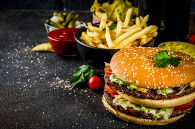 Çeşitli parti gıda, hamburger, patates kızartması, patates cipsi, salatalık turşusu, soğan, domates ve soğuk bira şişeleri, paslı siyah beton arka plan kopya alanı