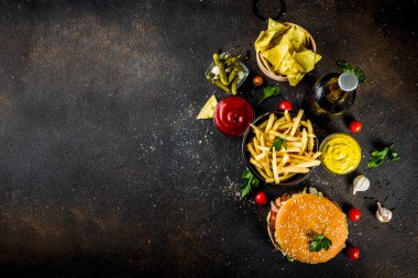 Çeşitli parti gıda, hamburger, patates kızartması, patates cipsi, salatalık turşusu, soğan, domates ve soğuk bira şişeleri, paslı siyah beton arka plan kopya alanı