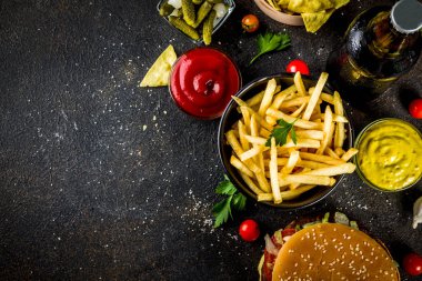 Çeşitli parti gıda, hamburger, patates kızartması, patates cipsi, salatalık turşusu, soğan, domates ve soğuk bira şişeleri, paslı siyah beton arka plan kopya alanı