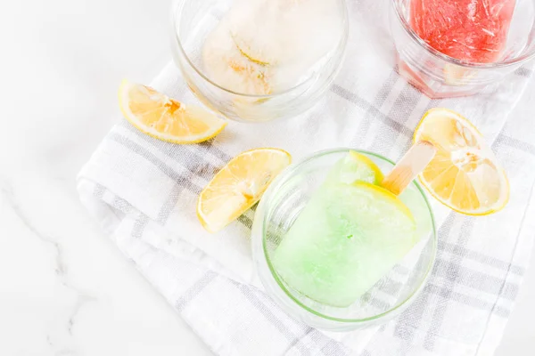 Summer party food ideas, frozen boozy alcohol cocktails popsicles - Prosecco, Vodka lime mojito, Champagne, Bellini, Margarita, Negroni etc white marble table copy space