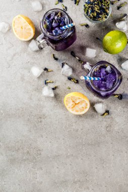 Sağlıklı yaz soğuk içecek, buzlu organik ve menekşe mavi kelebek bezelye çiçeği çayı limes ve limon, gri beton arka plan kopya alanı üstten görünüm