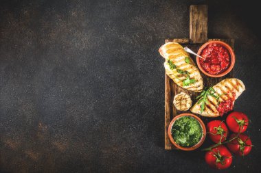 Izgara tavuk göğsü ile baharatlı sos, domates ve otlar üzerinde karanlık paslı arka plan kopya alanı üstten görünüm