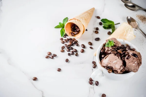 Homemade coffee ice cream, served with coffee beans and mint leaves, with ice cream cones and spoons in the picture. White marble background,