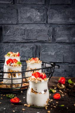 Sağlıklı yaz kahvaltı fikir, ev yapımı granola, yoğurt ve çilek, koyu arka plan kopya alanı ile küçük kavanoza parfe tatlı katmanlı.