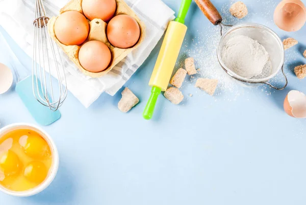 Ingredients and utensils for cooking baking egg, flour, sugar, whisk, rolling pin, on blue background, top view copy space