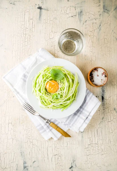 Trendy vegan food recipes, cheese zucchini spaghetti pasta with egg yolk with parmesan, olive oil and basil leaves, light concrete background copy space