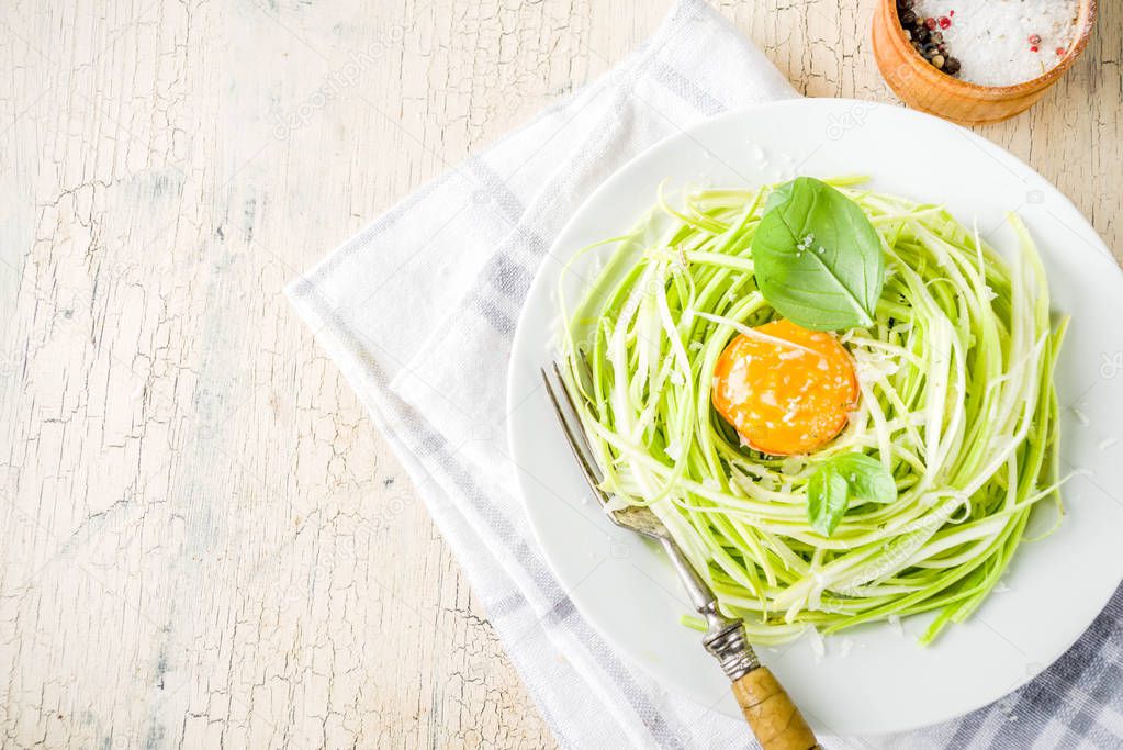 Trendy vegan food recipes, cheese zucchini spaghetti pasta with egg yolk with parmesan, olive oil and basil leaves, light concrete background copy space