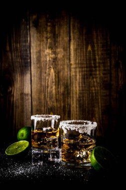İki tekila shot bardağı buz küpleriyle koyu arka plan üzerine tuz ve limes alanı Kopyala