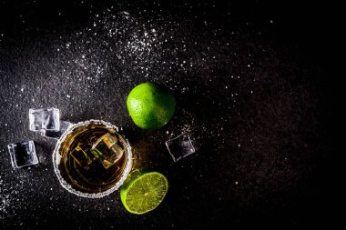 İki tekila shot bardağı buz küpleriyle koyu arka plan üzerine tuz ve limes alanı Kopyala